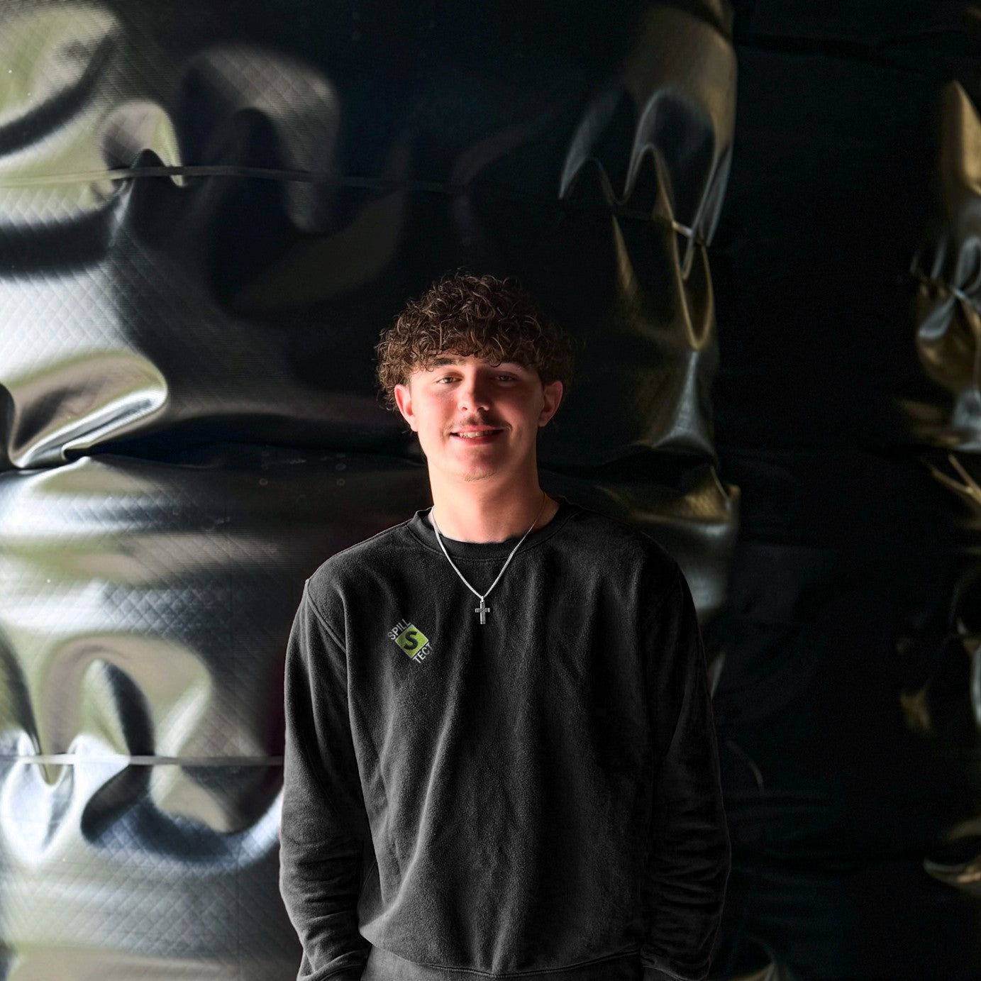 Person wearing a black sweatshirt with a logo in front of a graffiti wall.